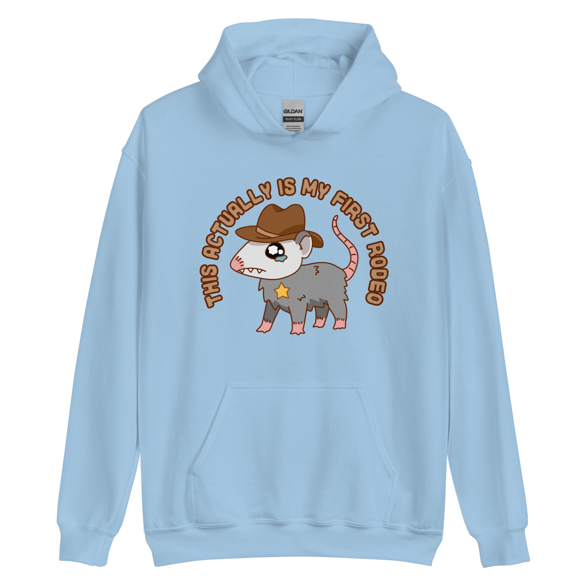 A light blue hooded sweatshirt featuring an illustration of a cute and nervous possum wearing a cowboy hat and sherrif's star badge. Text above the possum in an arc reads "this actually is my first rodeo".