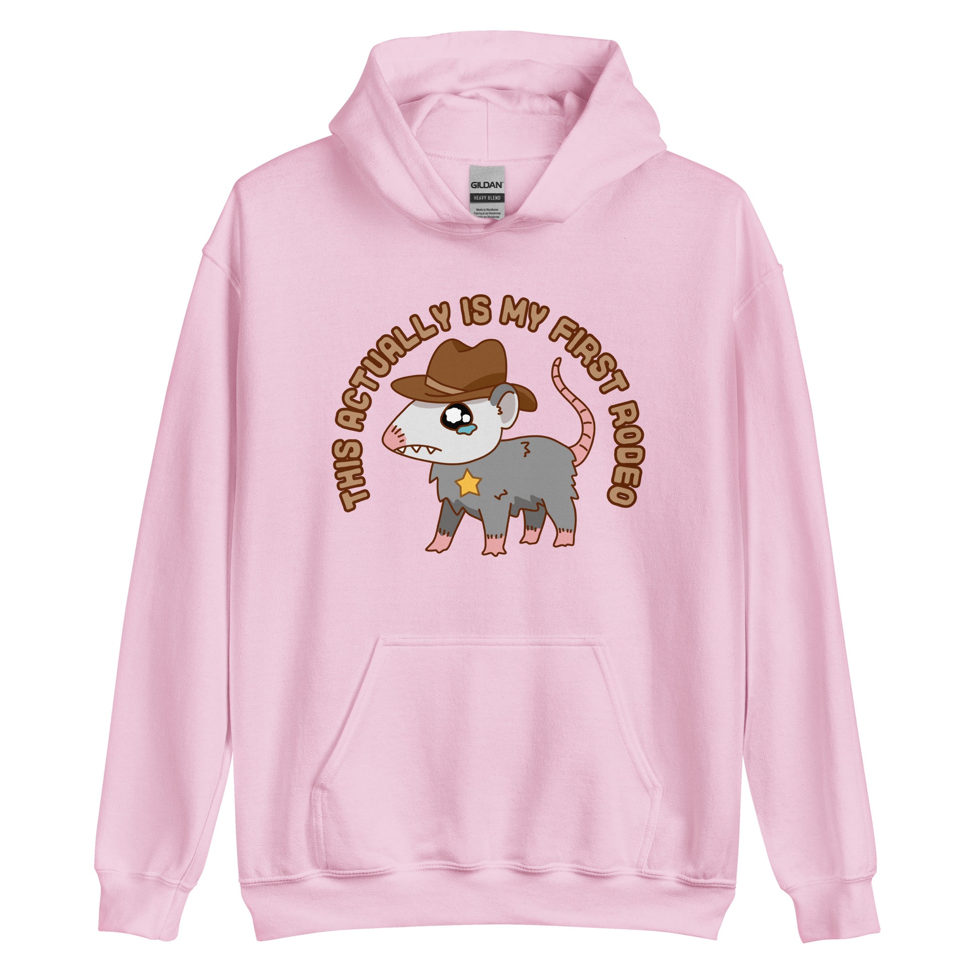 A light pink hooded sweatshirt featuring an illustration of a cute and nervous possum wearing a cowboy hat and sherrif's star badge. Text above the possum in an arc reads "this actually is my first rodeo".