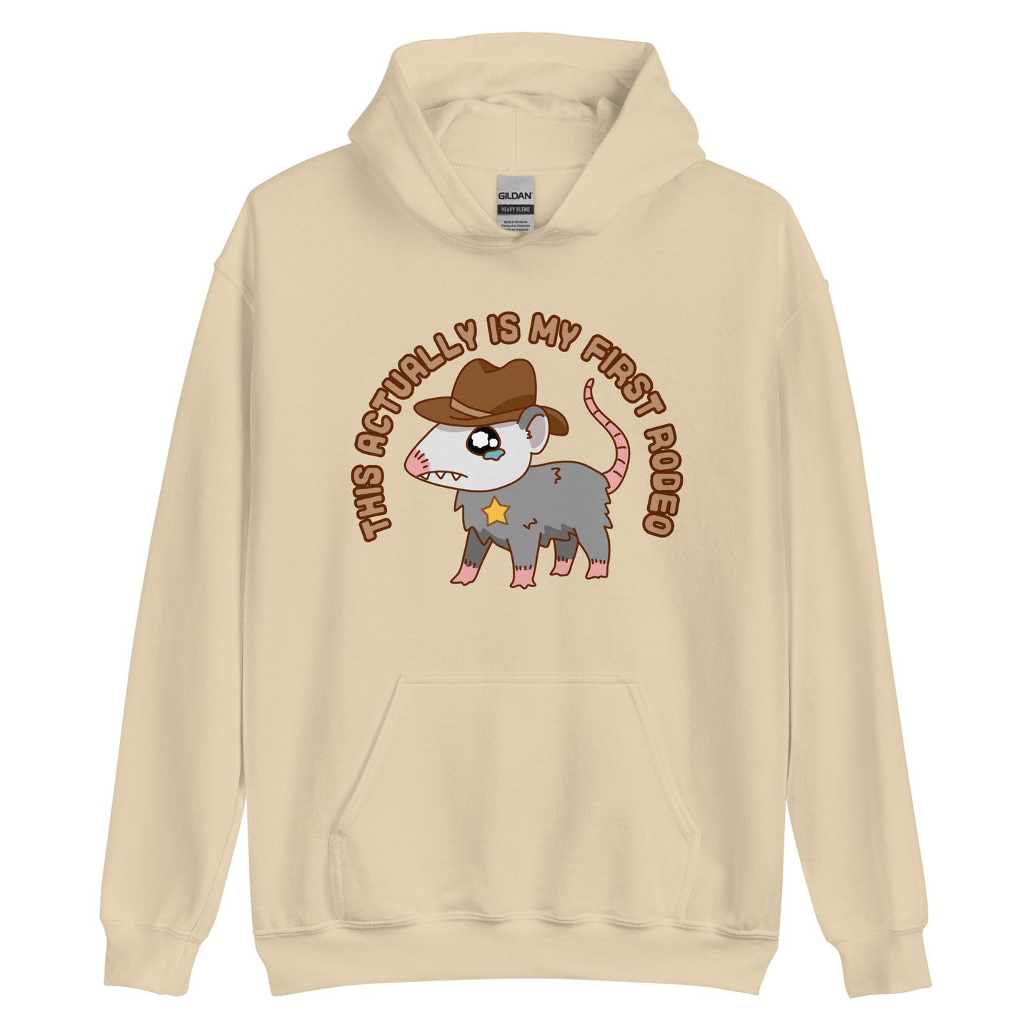 A tan-colored hooded sweatshirt featuring an illustration of a cute and nervous possum wearing a cowboy hat and sherrif's star badge. Text above the possum in an arc reads "this actually is my first rodeo".