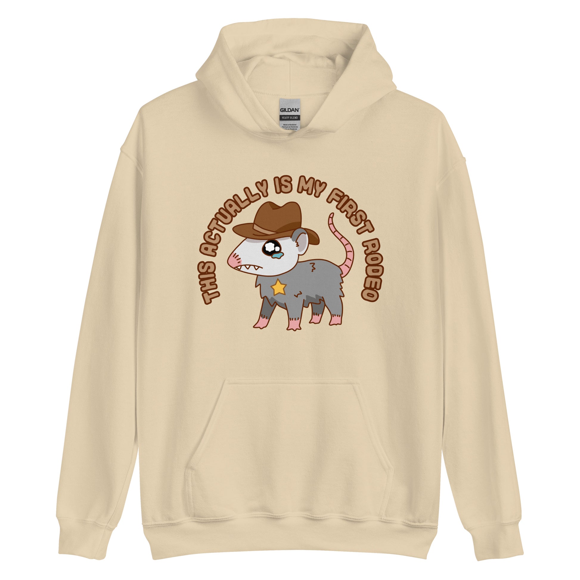 A tan-colored hooded sweatshirt featuring an illustration of a cute and nervous possum wearing a cowboy hat and sherrif's star badge. Text above the possum in an arc reads "this actually is my first rodeo".