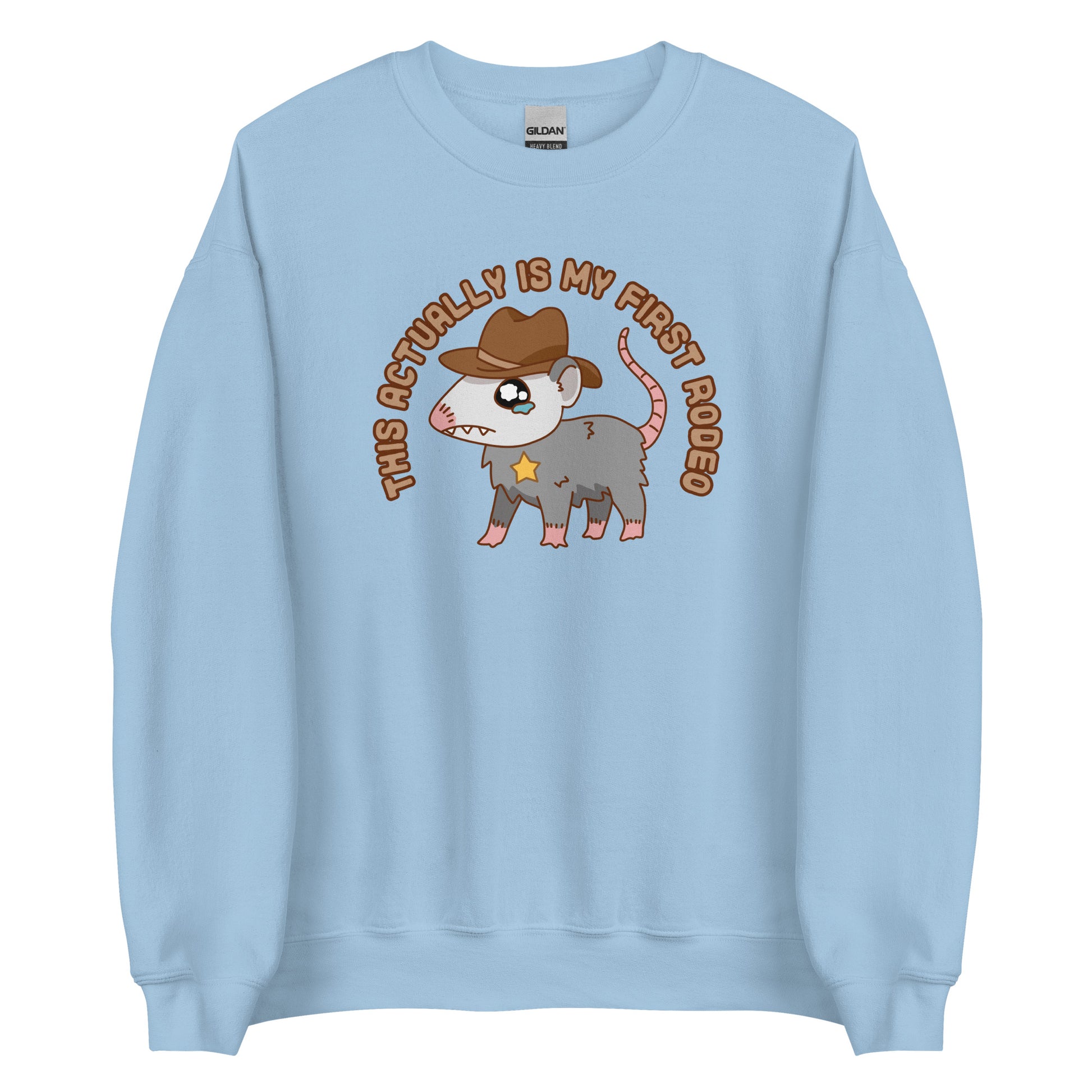 A light blue crewneck sweatshirt featuring an illustration of a cute and nervous possum wearing a cowboy hat and sherrif's star badge. Text above the possum in an arc reads "this actually is my first rodeo".