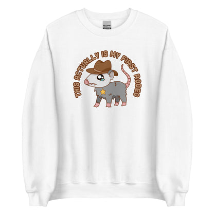 A white crewneck sweatshirt featuring an illustration of a cute and nervous possum wearing a cowboy hat and sherrif's star badge. Text above the possum in an arc reads "this actually is my first rodeo".