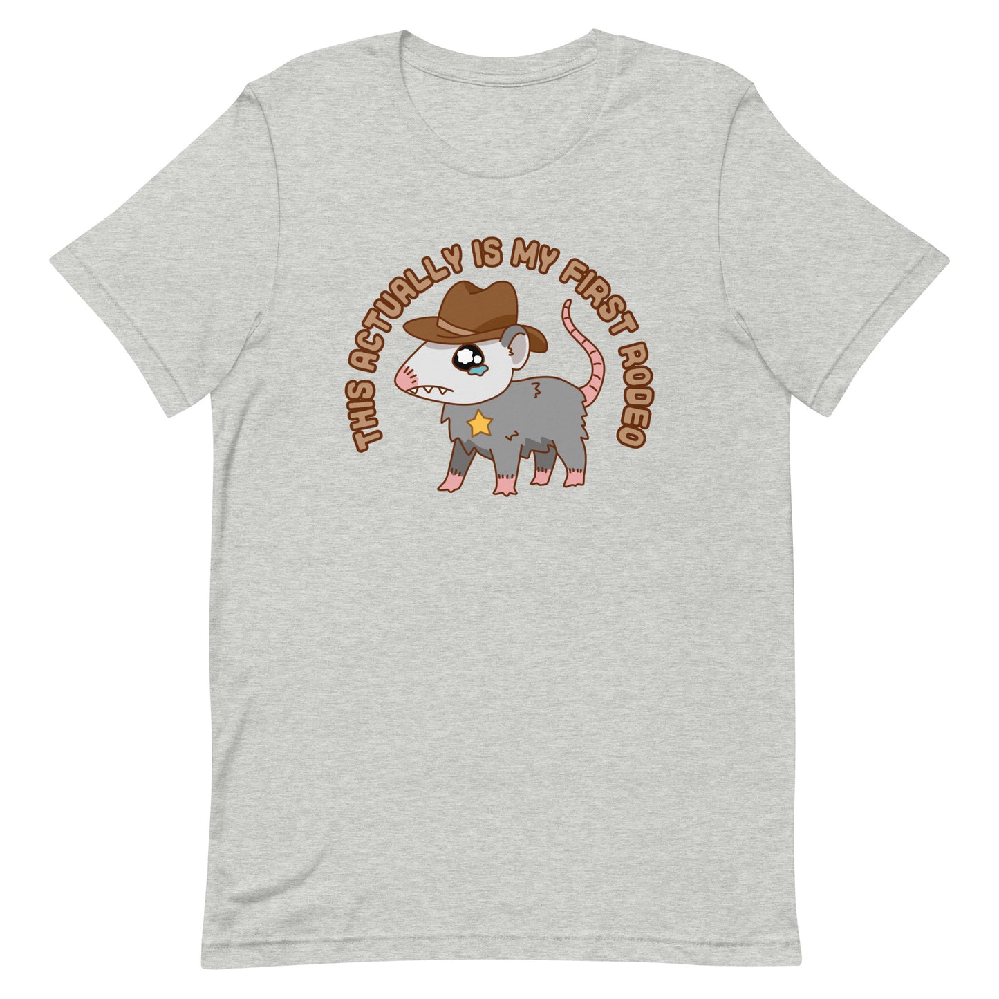 A grey crewneck t-shirt featuring an illustration of a cute and nervous possum wearing a cowboy hat and sherrif's star badge. Text above the possum in an arc reads "this actually is my first rodeo".