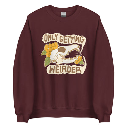 A maroon crewneck sweatshirt featuring an illustration of a fox skull surrounded by yellow flowers. Wobbly speech bubbles are coming from the fox's mouth. The text inside the bubbles reads "ONLY GETTING WEIRDER".