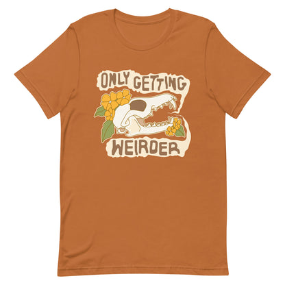 A burnt orange t-shirt featuirng an illustration of a fox skull surrounded by yellow flowers. Wobbly speech bubbles are coming from the fox's mouth. Text inside the bubbles reads "ONLY GETTING WEIRDER'.