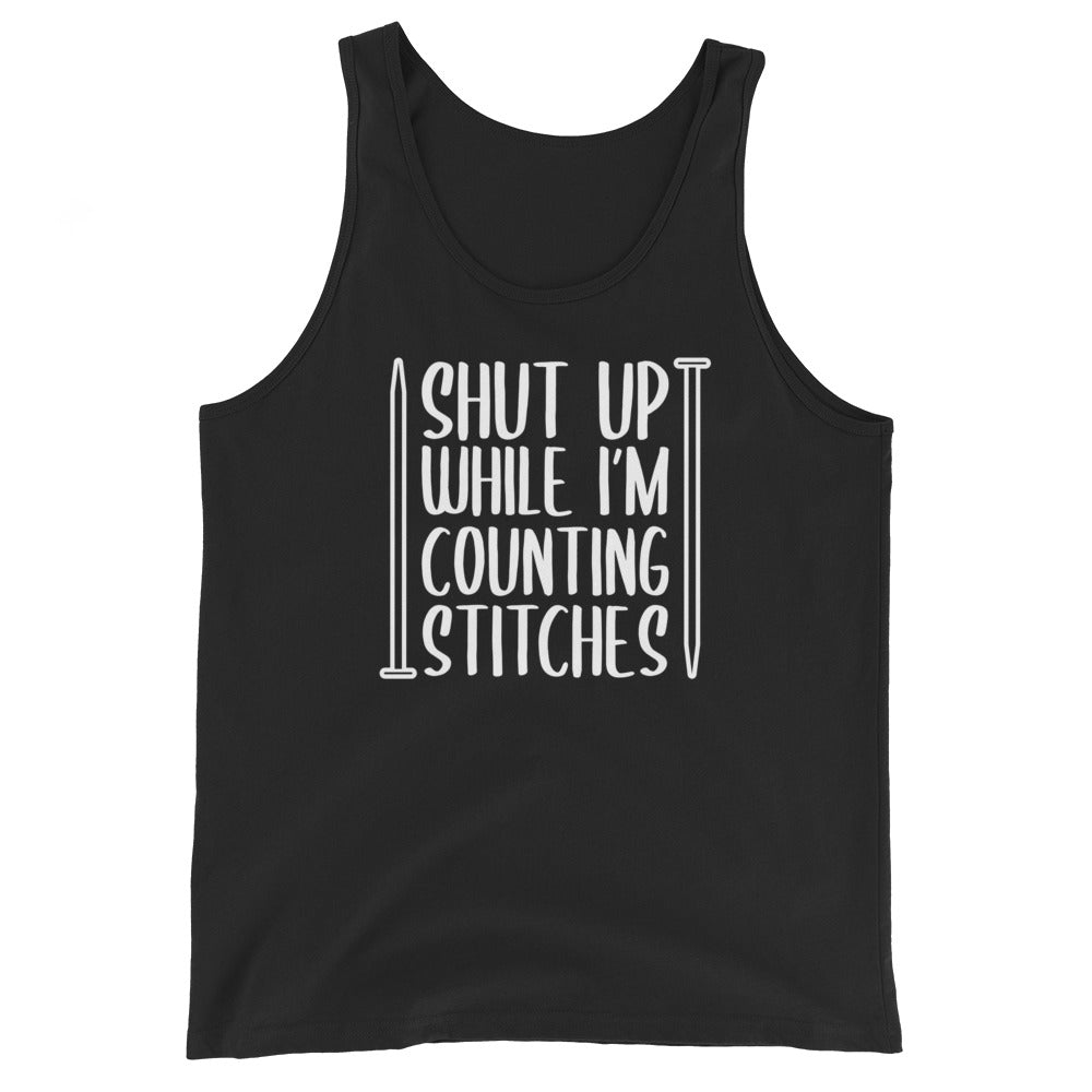 A black tank top with white text surrounded by two knitting needles. The text reads "Shut up while I'm counting stiches".