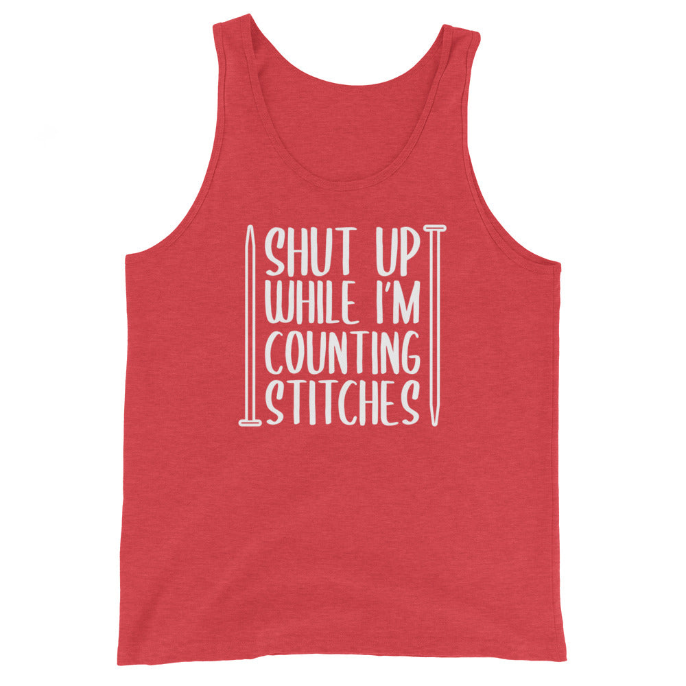 A red tank top with white text surrounded by two knitting needles. The text reads "Shut up while I'm counting stiches".