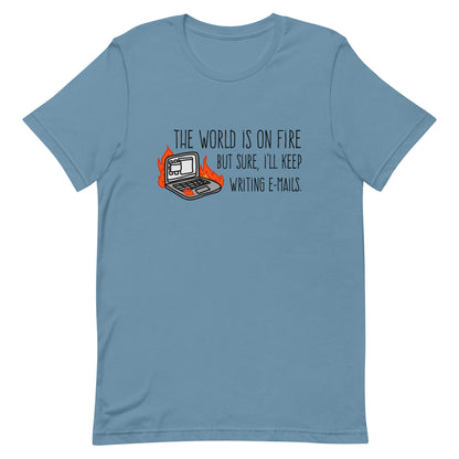 A blue crewneck t-shirt featuring a squiggly illustration of a laptop that is on fire. Text alongside the laptop reads "the world is on fire but sure, I'll keep writing e-mails."