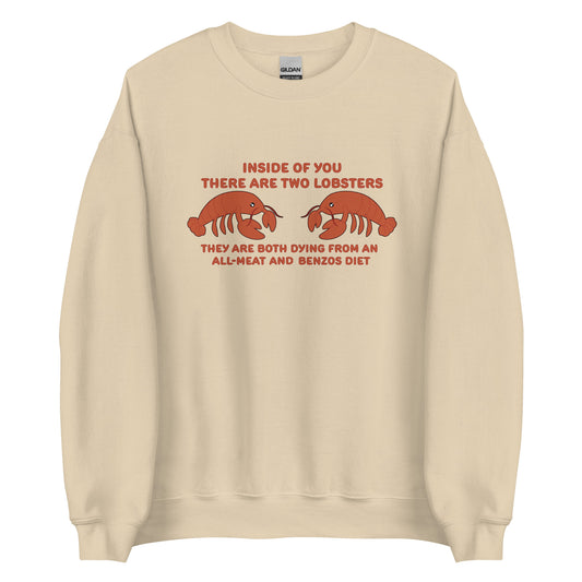 A tan crewneck sweatshirt featuring an illustration of two lobsters. Text around the lobsters reads "Inside of you there are two lobsters. They are both dying from an all-meat and benzos diet."