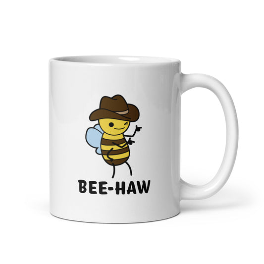 A white ceramic mug with an image of a bee in a cowboy hat on it. The bee is winking and holding up "finger guns". Text beneath the bee reads "Bee-Haw"