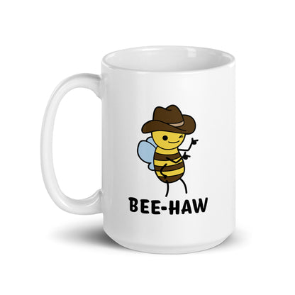 A 15 ounce white ceramic mug with an image of a bee in a cowboy hat on it. The bee is winking and holding up "finger guns". Text beneath the bee reads "Bee-Haw"