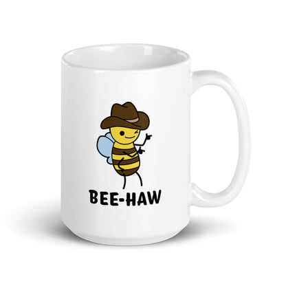 A 15 ounce white ceramic mug with an image of a bee in a cowboy hat on it. The bee is winking and holding up "finger guns". Text beneath the bee reads "Bee-Haw"
