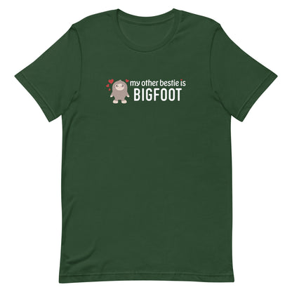 A forest green crewneck t-shirt featuring a cutesy illustration of Bigfoot, surrounded by hearts. Text alongside Bigfoot reads "my other bestie is Bigfoot"
