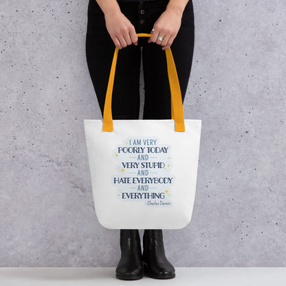 A wasit-down image of a model wearing all black and holding a white canvas tote bag. The bag has yellow handles and a quote from Charles Darwin in blue text. The quote reads "I am very poorly today and very stupid and hate everybody and everything".