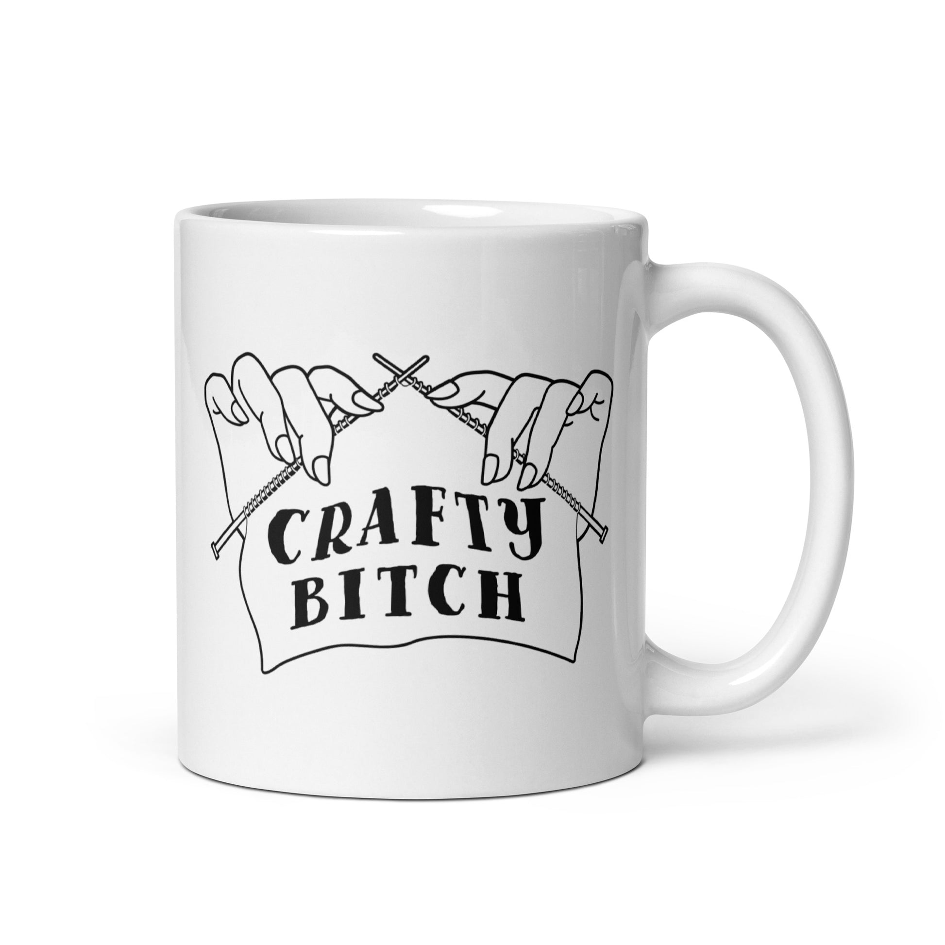 A white ceramic 11 ounce coffee mug featuring a single-color illustration of a pair of hands holding knitting needles. Fabric on the needles features text that reads "crafty bitch".