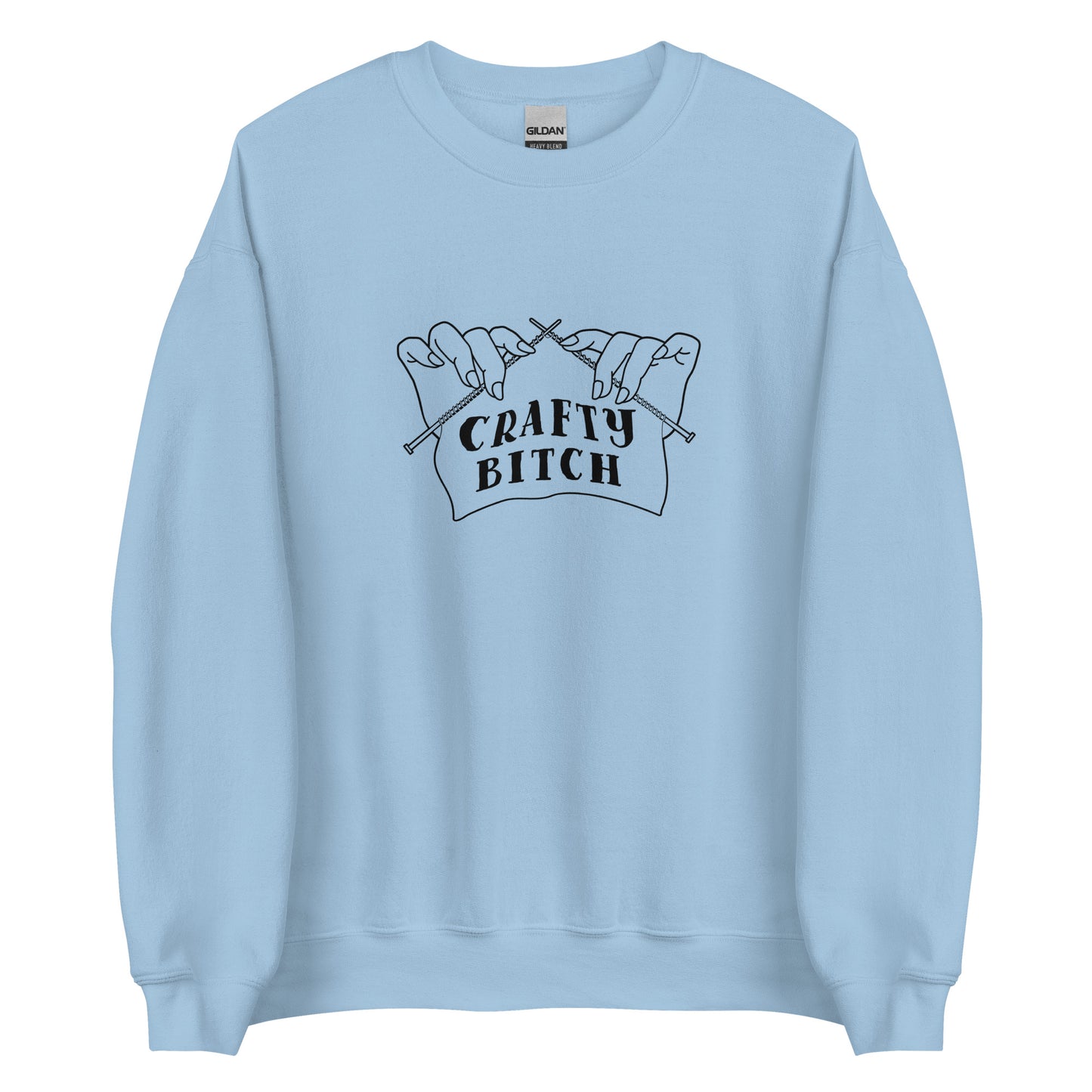 A light blue crewneck sweatshirt featuring a single-color illustration of a pair of hands holding knitting needles. Fabric on the needles features text that reads "crafty bitch".