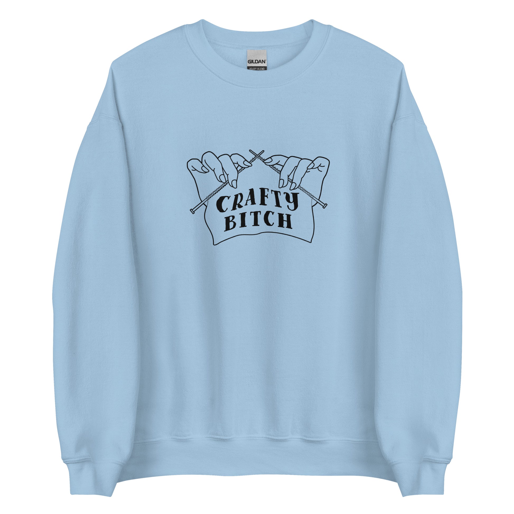 A light blue crewneck sweatshirt featuring a single-color illustration of a pair of hands holding knitting needles. Fabric on the needles features text that reads "crafty bitch".