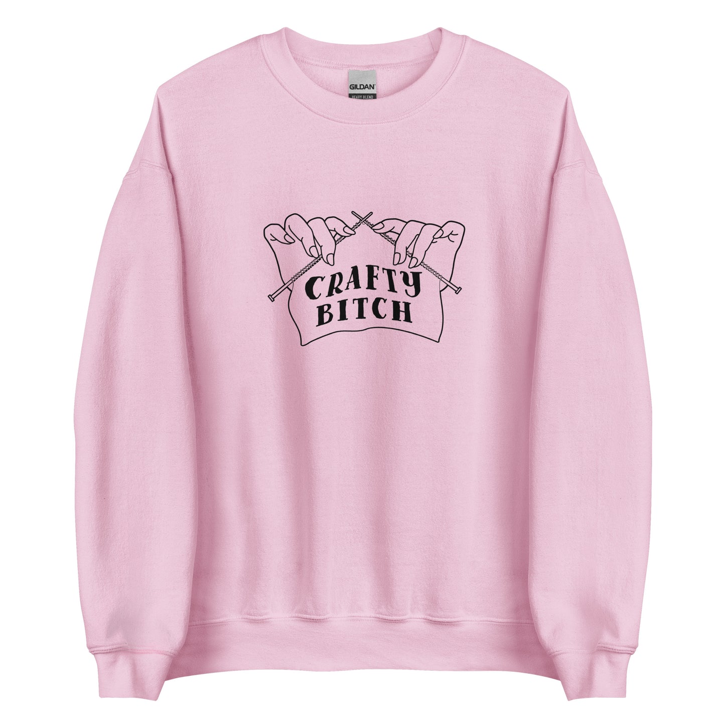 A light pink crewneck sweatshirt featuring a single-color illustration of a pair of hands holding knitting needles. Fabric on the needles features text that reads "crafty bitch".