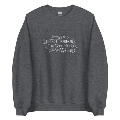 A dark heather grey crewneck sweatshirt with white old-fashioned text that reads "Be The Eldritch Horror You Wish To See In The World"