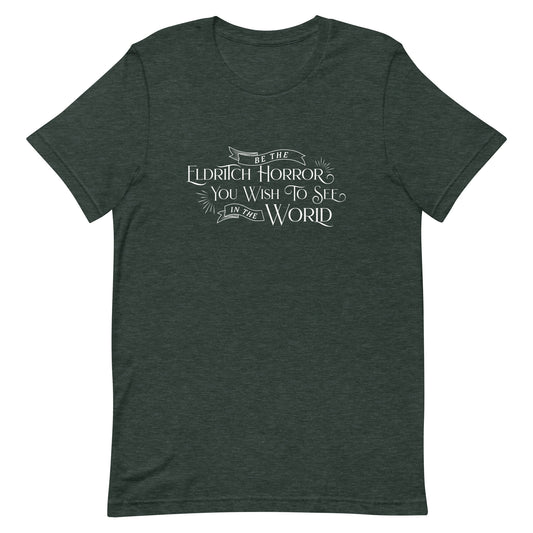 A dark heather green crewneck t-shirt with white text in an old-fashioned style that reads "Be The Eldritch Horror You Wish To See In The World"