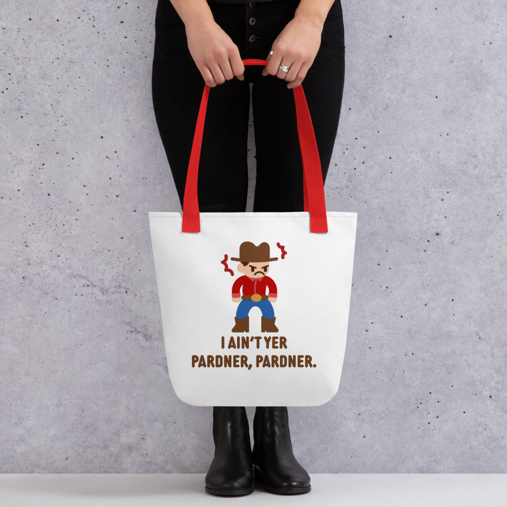 A waist-down image of a model wearing all-black. The model is holding a white canvas tote bag with a red handle featuring an illustration of a grumpy cowboy wearing a red shirt. Text alongside the cowboy reads "I ain't yer pardner, pardner."