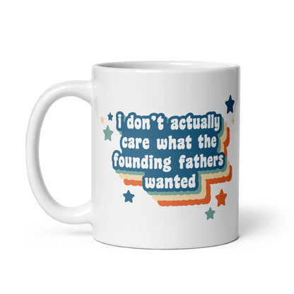 A white 11oz ceramic mug featuring text that reads "I don't actually care what the founding fathers wanted". Stars and a colorful drop shadow surround the text.