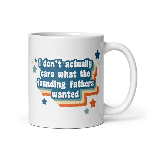 A white 11oz ceramic mug featuring text that reads "I don't actually care what the founding fathers wanted". Stars and a colorful drop shadow surround the text.