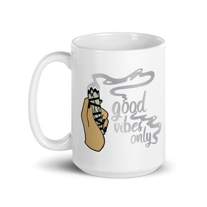 A 15 ounce white ceramic coffee mug featuring an illustration of a hand holding a sage smudge stick. Smoke flows from the tip of the sage and forms words that read "good vibes only"