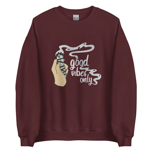 A maroon crewneck sweatshirt featuring an illustration of a hand holding a sage smudge stick. Smoke flows from the tip of the sage and forms text reading "Good vibes only"