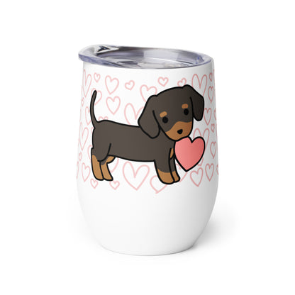 A white metal wine tumbler with a plastic lid. A pattern of hearts wraps around the top half of the tumbler. Centered on the tumbler is a cute, stylized illustration of a Dachschund.
