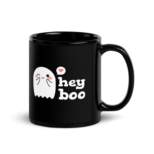 A black 11 ounce coffee mug featuring an illustration of a blushing and smiling ghost next to text that reads "hey boo"