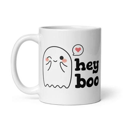 A white 11 ounce coffee mug featuring an illustration of a blushing and smiling ghost next to text that reads "hey boo"
