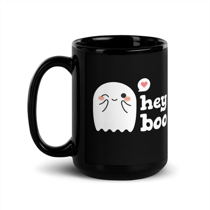 A black 15 ounce coffee mug featuring an illustration of a blushing and smiling ghost next to text that reads "hey boo"