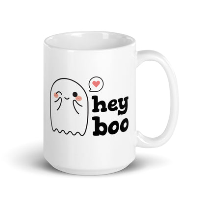 A white 15 ounce coffee mug featuring an illustration of a blushing and smiling ghost next to text that reads "hey boo"