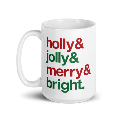 A white 15 ounce ceramic mug with four lines of red and green text that read "Holly & Jolly & Merry & Bright"