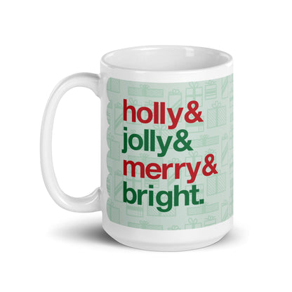 A 15 ounce ceramic mug with four lines of red and green text on a background pattern of light green presents of various sizes. The text on the mug reads "Holly & Jolly & Merry & Bright".