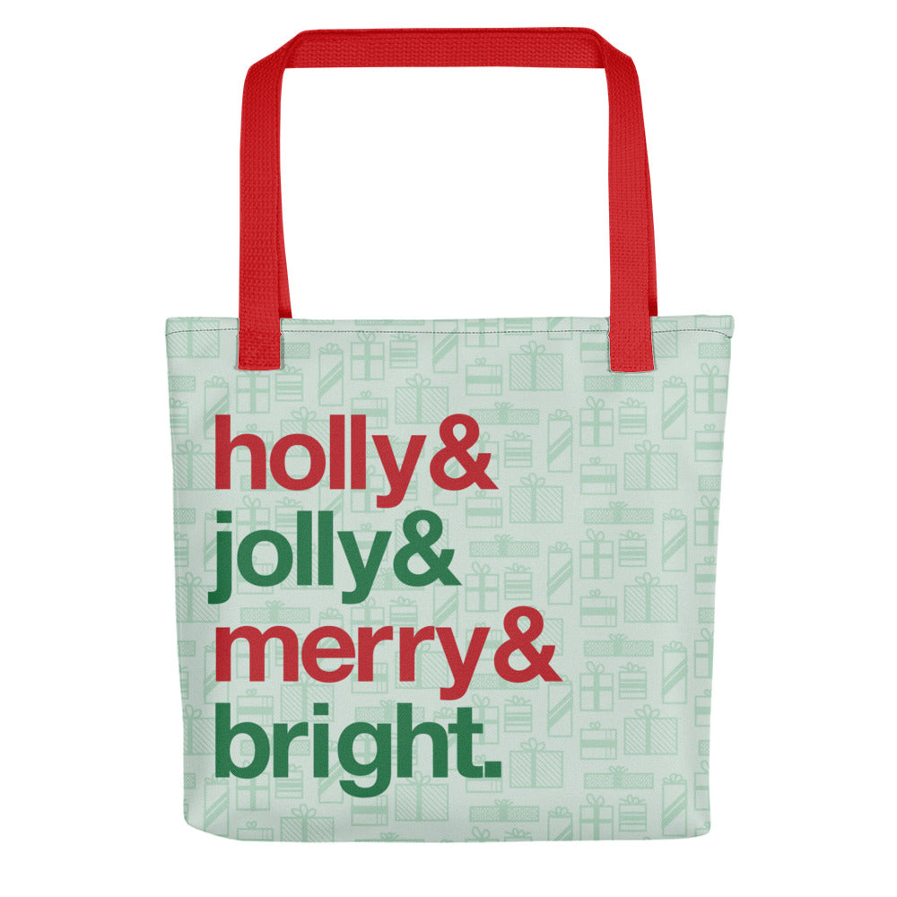 A tote bag with red handles and a printed pattern of light green presents of various sizes. There are also four lines of red and green text on the bag that read "Holly & jolly & merry & bright"