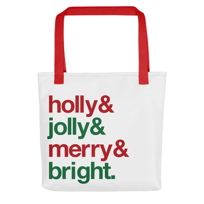 A white tote bag with red handles, decorated with four lines of red and green text. The text reads "Holly & jolly & merry & bright."