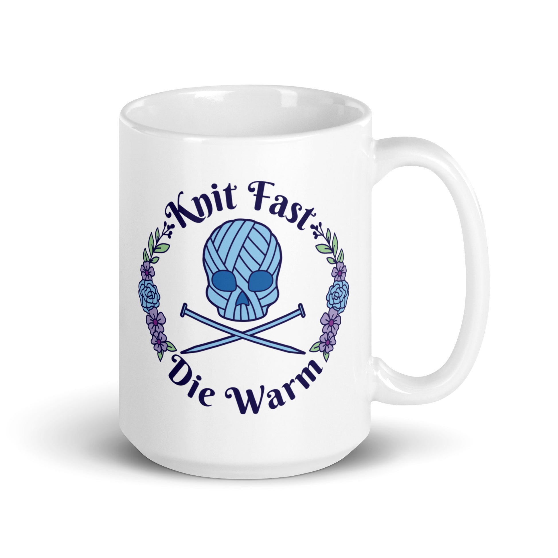 A white 15 ounce mug featuring an image of a blue skull and crossbones made of yarn and knitting needles. A floral wreath surrounds the skull, along with words that read "Knit Fast, Die Warm"