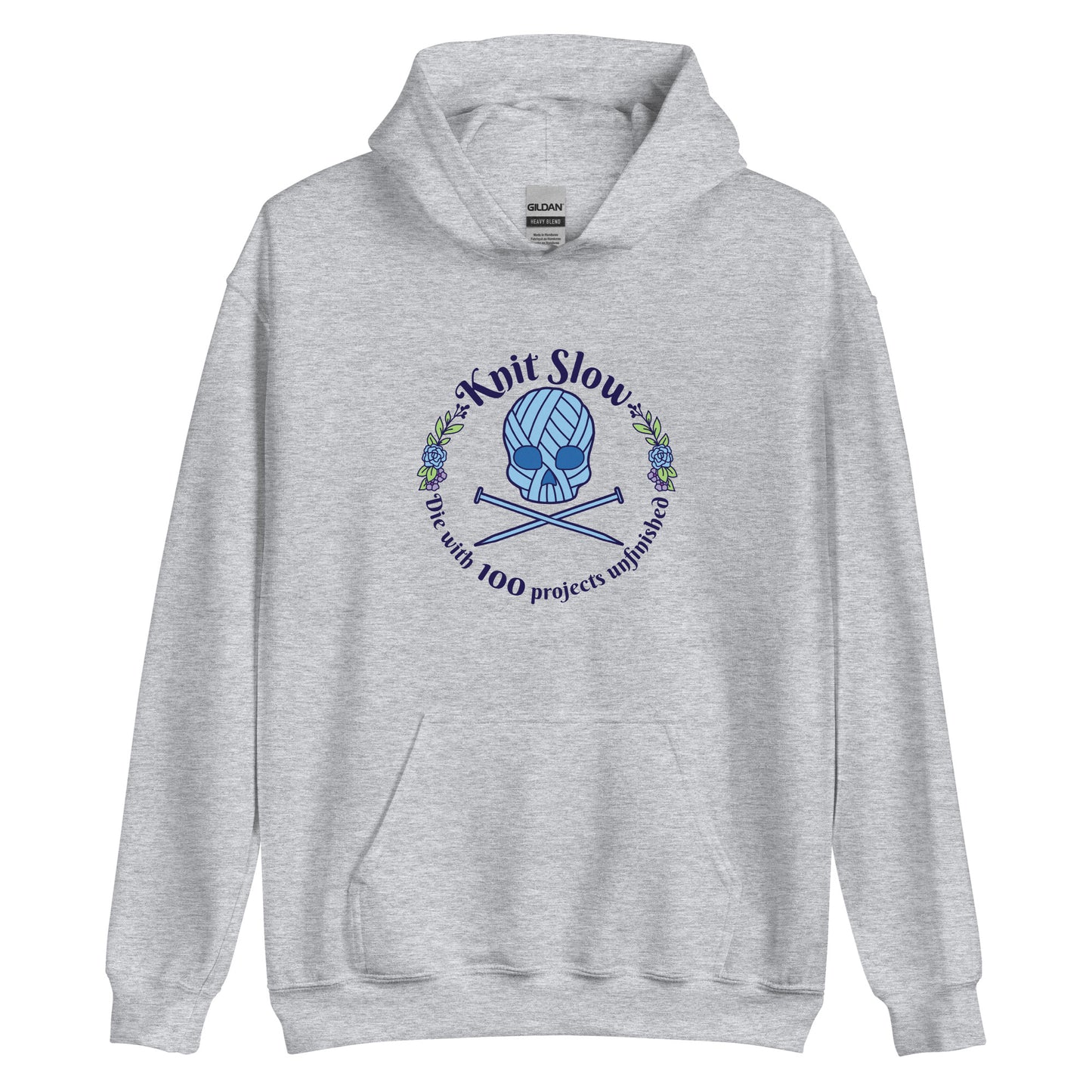 A grey hooded sweatshirt featuring an image of a skull and crossbones made of yarn and knitting needles. A floral wreath surrounds the skull, along with words that read "Knit Slow, Die with 100 projects unfinished"