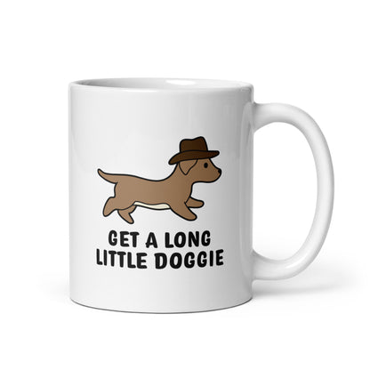 A white 11 ounce ceramic mug featuring an image of a dachshund wearing a cowboy hat. Text below the dog reads "Get a long little doggie"