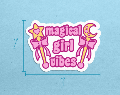 A diecut sticker featuring two gold wands with pink bows and pink text reading "Magical girl vibes" next to measurements reading 2" high and 3" wide