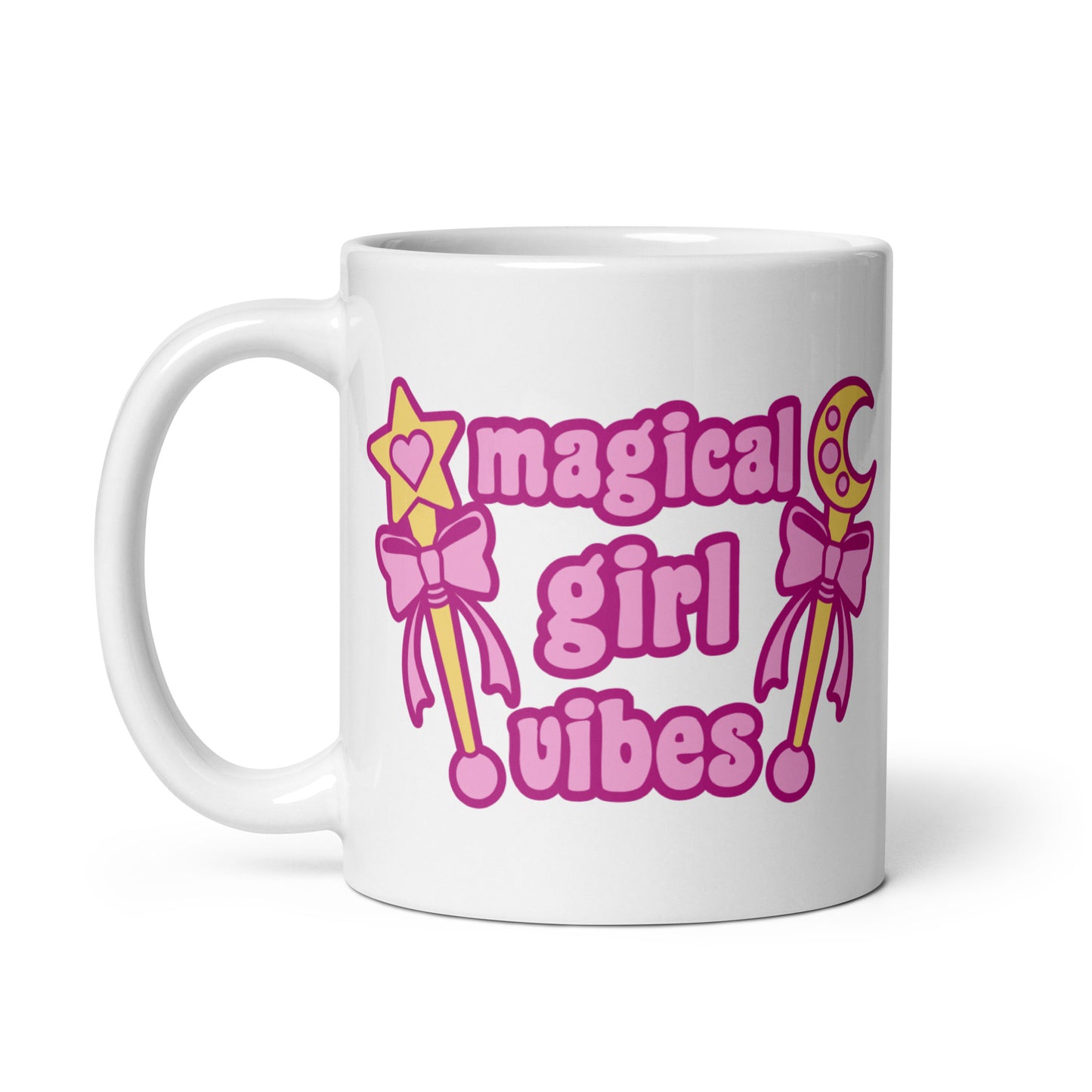 An 11 oz white ceramic mug with the handle to the left featuring two gold wands with pink bows and pink text reading "Magical girl vibes"