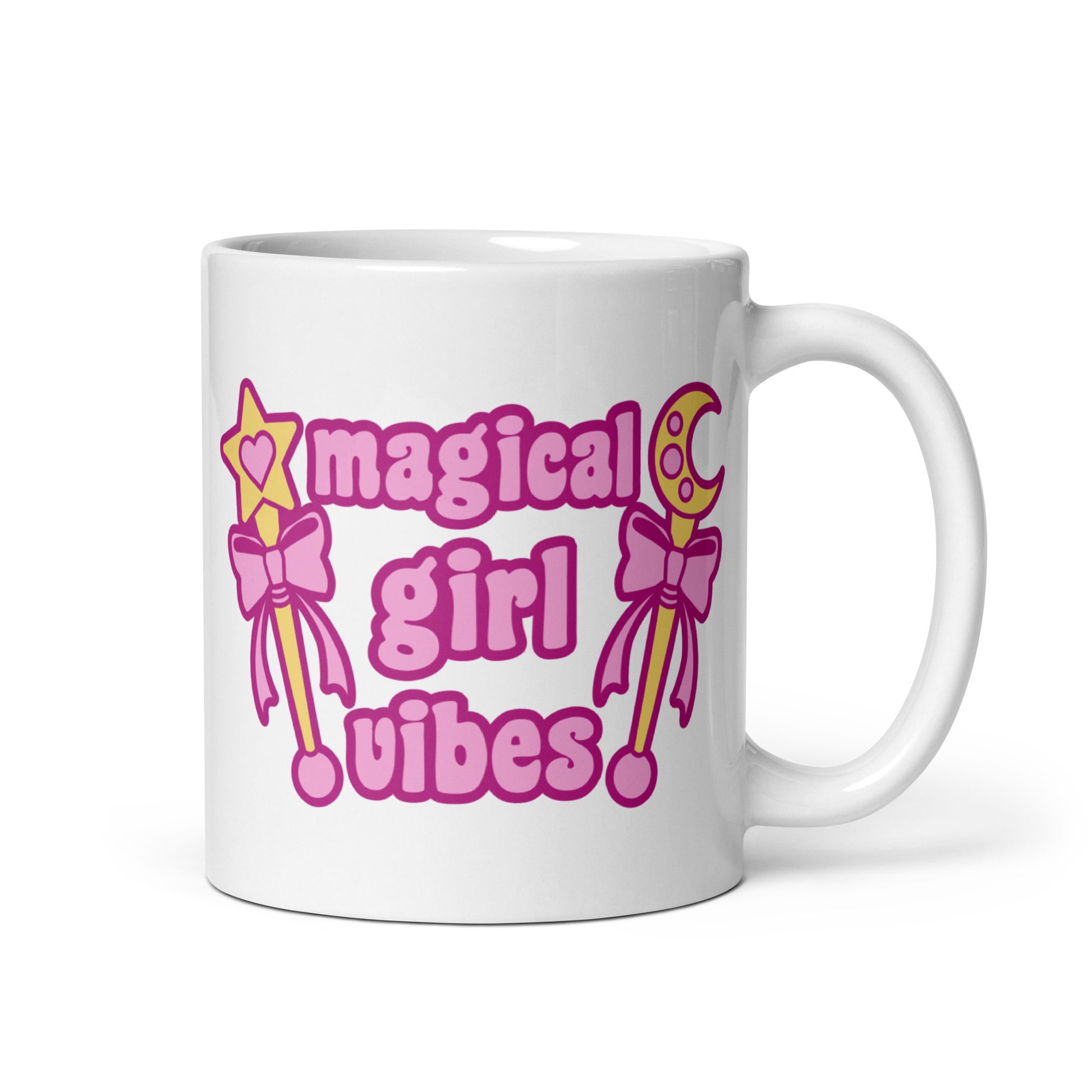 An 11 oz white ceramic mug with the handle to the right featuring two gold wands with pink bows and pink text reading "Magical girl vibes"