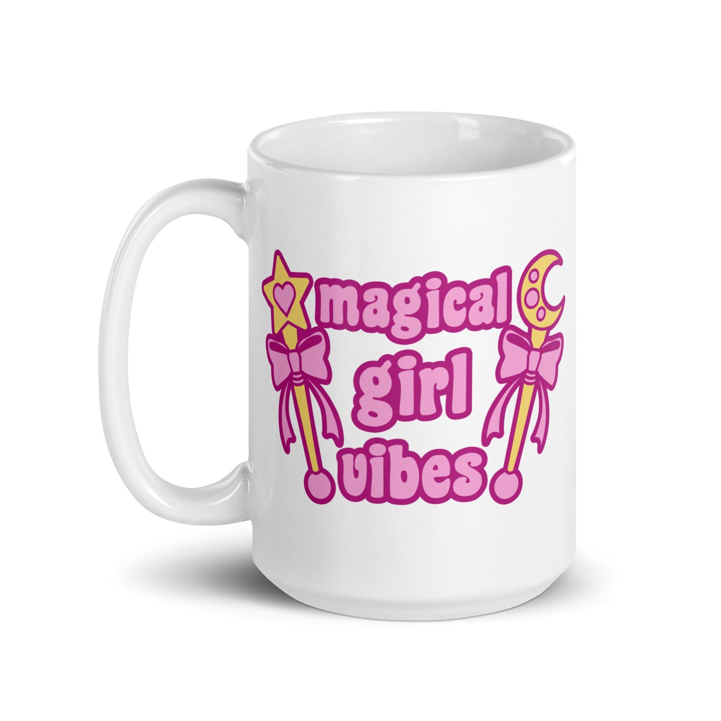 An 15 oz white ceramic mug with the handle to the left featuring two gold wands with pink bows and pink text reading "Magical girl vibes"