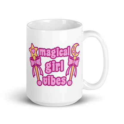 An 15 oz white ceramic mug with the handle to the right featuring two gold wands with pink bows and pink text reading "Magical girl vibes"
