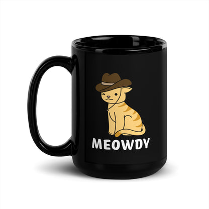 A black 15 ounce ceramic coffee mug featuring an illustration of an orange striped cat wearing a cowboy hat. The cat is winking and smiling, and text beneath him reads "Meowdy"