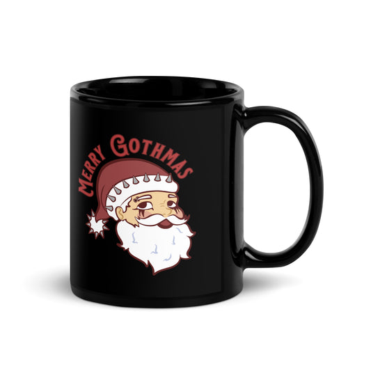 A black ceramic coffee mug featuring an image of Santa Claus. Santa's hat has spikes on it and he is wearing goth-style makeup. Text above Santa's head reads "Merry Gothmas"