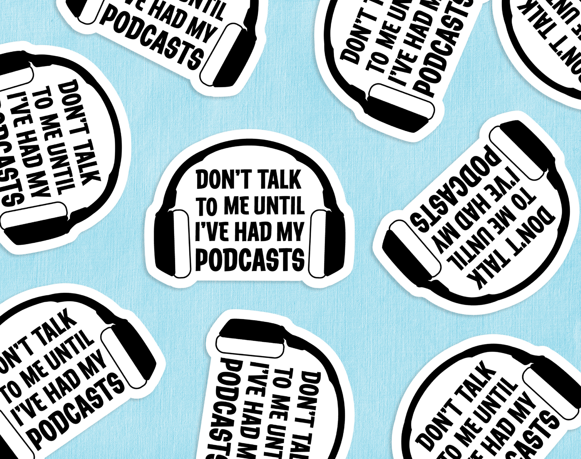 A group of die-cut stickers featuring headphones and text reading "Don't talk to me until I've had my podcasts" scattered across a blue paper backdrop