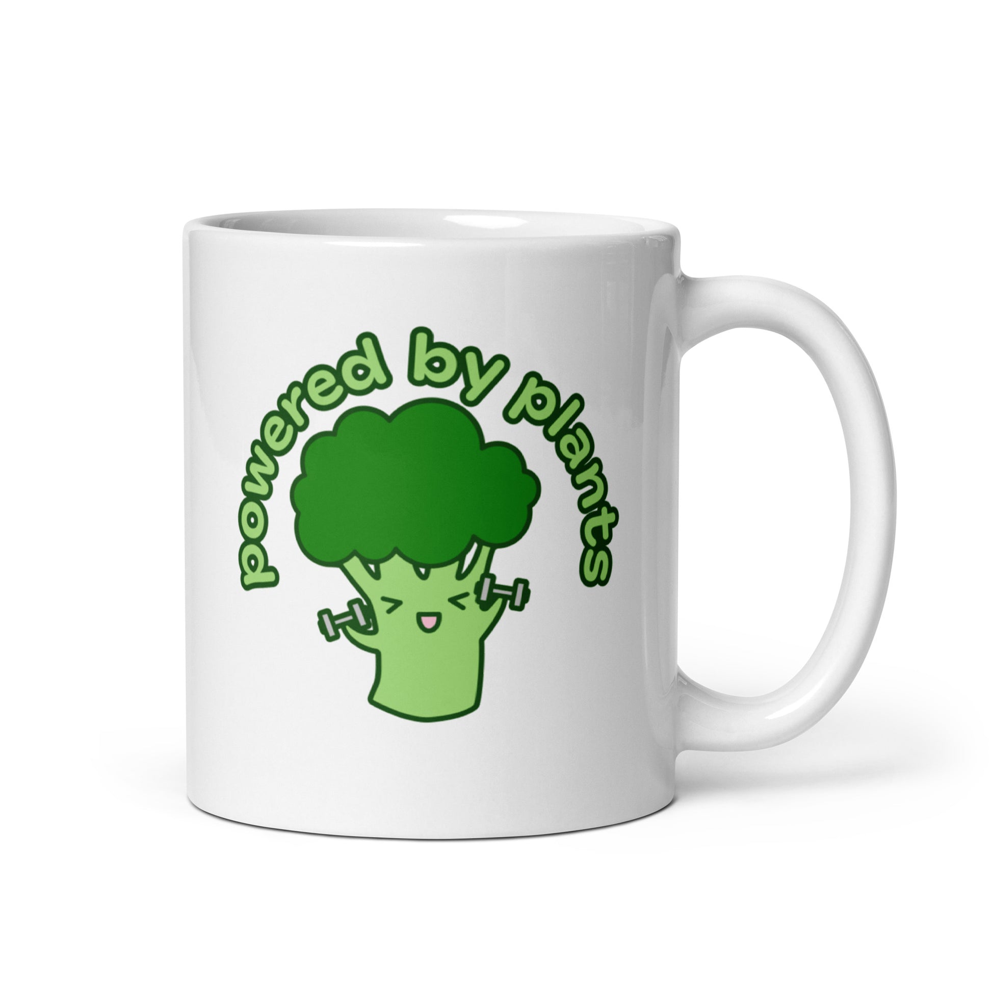 A white 11 ounce ceramic coffee mug featuring a cute illustration of a cartoon broccoli. The broccoli is excitedly lifting weights and text above him in an arc reads "powered by plants".